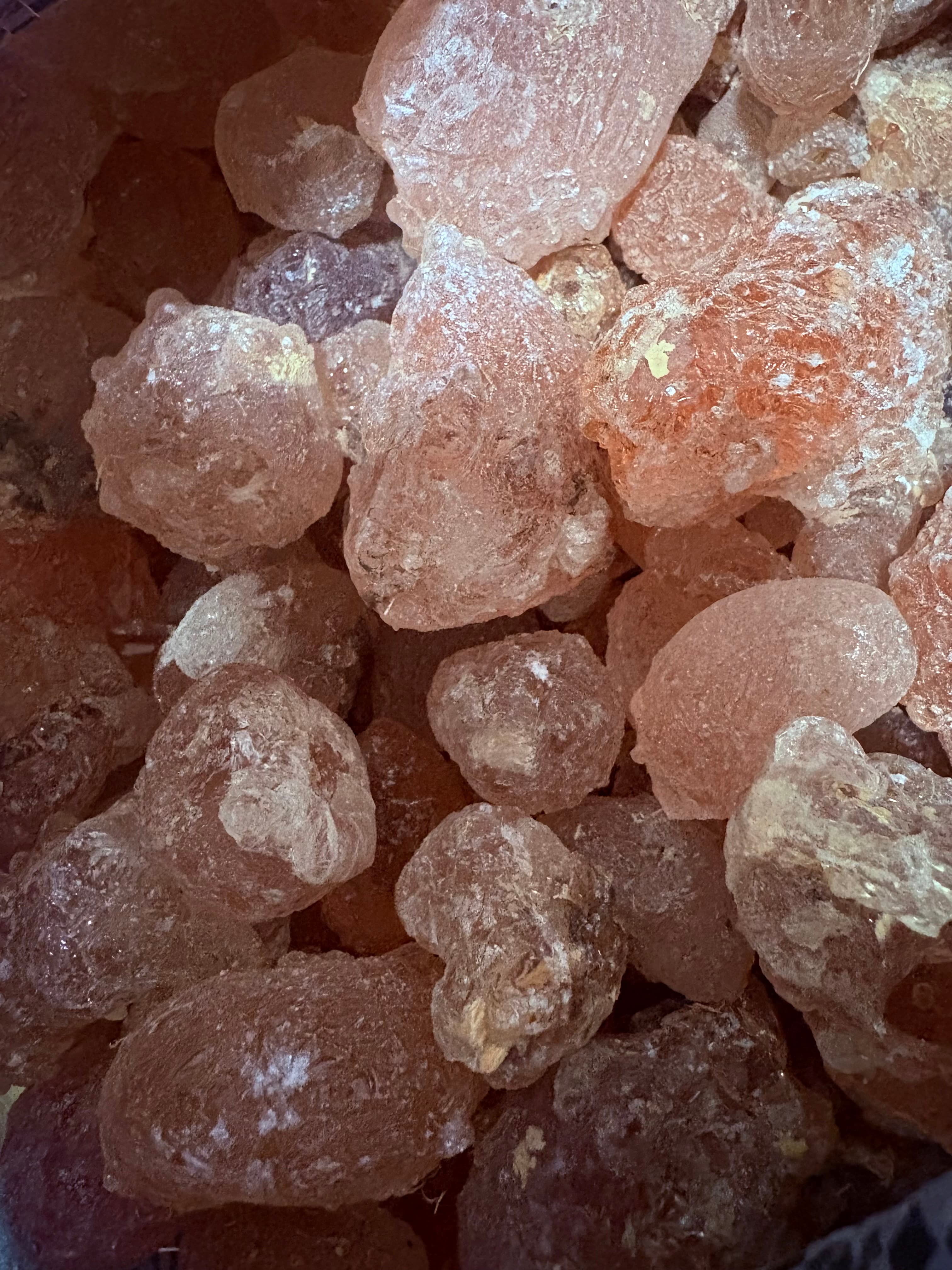 Close-up of translucent, amber-colored gum arabic crystals with irregular shapes and powdery surfaces.